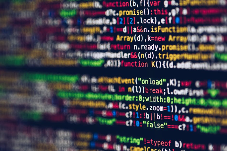 A person using a laptop on a dark surface, the screen displaying lines of code with colorful syntax highlighting, suggesting programming or web development activity. The person's hands are visible, wi